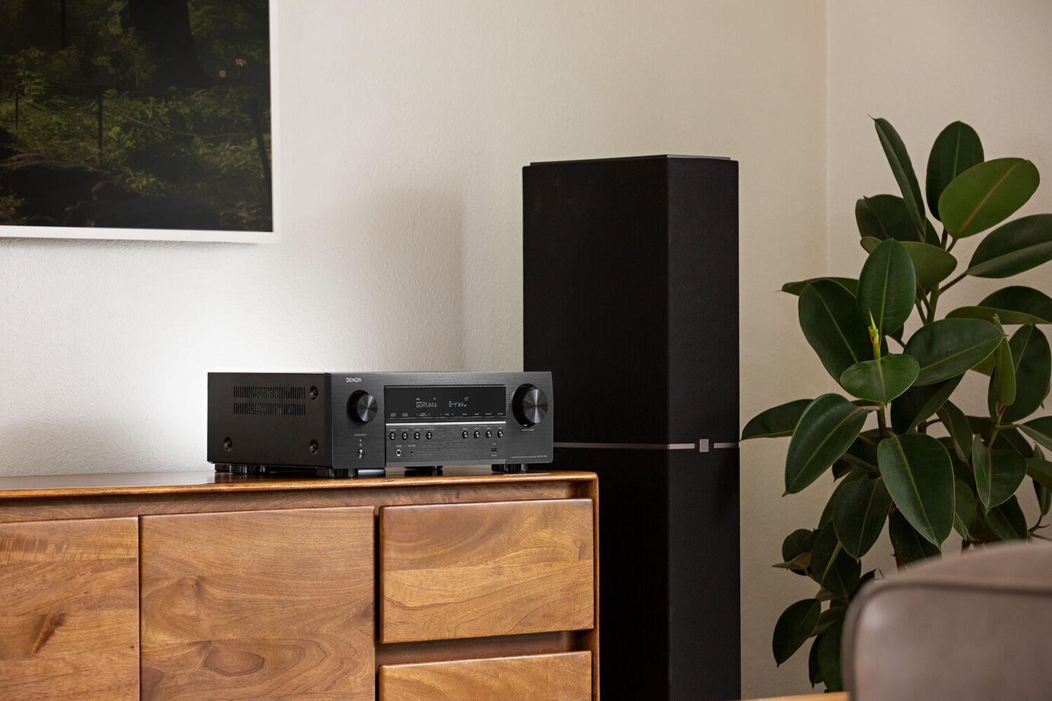 An S-Series AVR on a tv stand next to a floor standing speaker